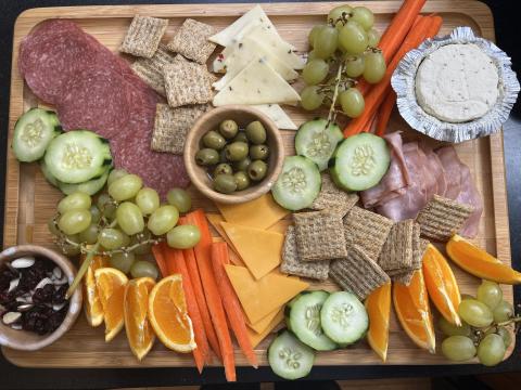 A charcuterie board with olives, cheese, meats, carrots, cucumbers, fruit, and crackers